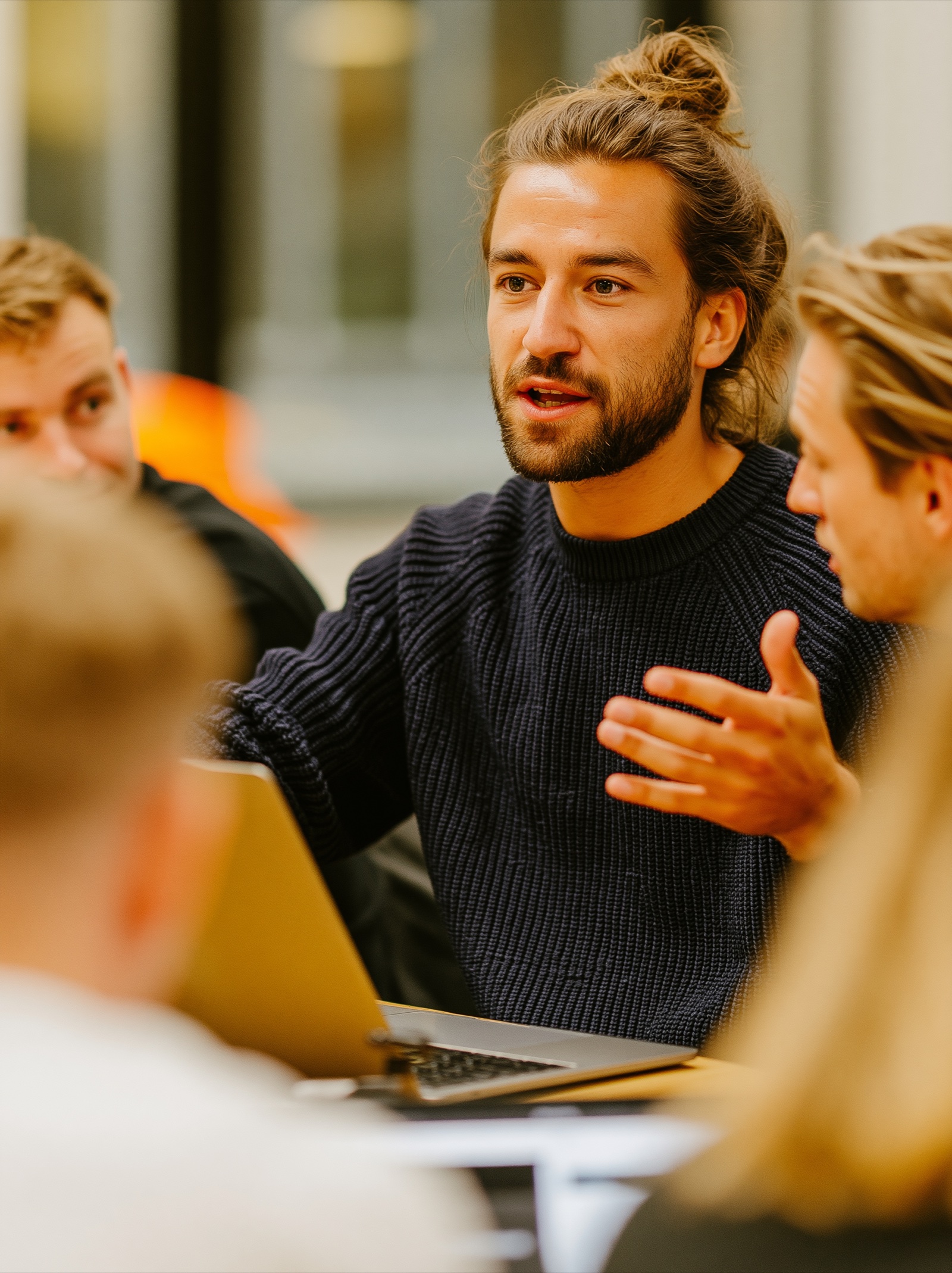 A consultant mid-conversation at a laptop with colleagues around the table